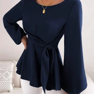 Mörkblå blus med knytband - Elegant mörkblå blus med långa ärmar och ett knytband i midjan. Blusen har en rund halsringning och vida ärmar som ger en stilfull look.