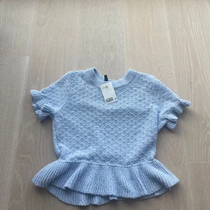 Ljusblå stickad topp med volanger  - - Söt ljusblå stickad topp med korta ärmar och volangdetalj vid nederkanten. Denna topp är i storlek M men passar S/ XS också! 50 kr + frakt, aldrig använd ( lappen är även kvar)