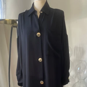 Svart skjort/blus  från Zara - Elegant svart oversize skjorta  från Zara med stora guldknappar framtill,  långa ärmar och en klassisk krage. Perfekt för en stilren look. Storlek S oversize modell så passar större storlek med