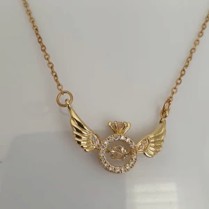 Guldhalsband med vingmotiv - Elegant guldhalsband med ett unikt hängsmycke i form av vingar och en cirkel dekorerad med glittrande stenar. Perfekt för att ge en touch av glamour till din stil.