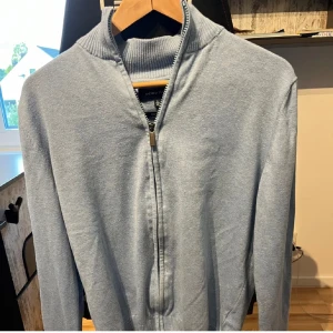 Ljusblå kofta från Andrew James - Säljer en ljusblå kofta från Andrew James i ekologisk bomull. Koftan har en dragkedja framtill och ribbade muddar vid ärmslut och nederkant. Perfekt för en stilren och bekväm look. Skick 10/10 och passar mellan 170-155 cm och 65-55 kg😇