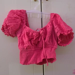 Rosa blus med spetsdetaljer - Charmig rosa blus med spetsdetaljer och puffiga kortärmar. Den har en söt knytning framtill och en elastisk midja för en bekväm passform. Perfekt för en somrig look!