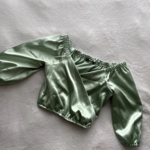 Grön satinblus från Bik Bok - Snygg grön satinblus från Bik Bok med offshoulder-design. Blusen har långa ärmar och elastiska kanter för en bekväm passform. Perfekt för en stilren look. Blusen är en kort topp som passar super till sommaren