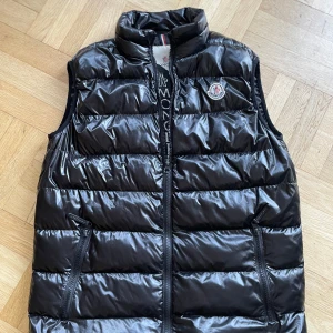 Svart dunväst från Moncler - Snygg svart dunväst från Moncler med dragkedja och hög krage. Västen har ett stilrent quiltat mönster och Monclers logotyp på bröstet. Okej skick. Kan tänka mig att byta mot annat t.ex Patagonia.