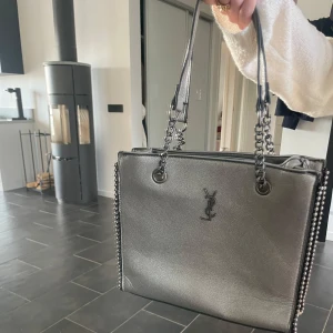 Silverfärgad axelväska från YSL - Silver färgad axelväska från Ysl. Oklart om den är äkta därför ett billigt pris. Väskan har många innerfack i väskan och är väldigt smidig att ta med sig. Säljer pga att jag inte använder den💘