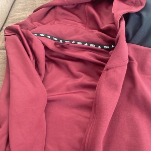 Vinröd hoodie från Adidas - Säljer en snygg vinröd hoodie från Adidas. Perfekt för yoga eller avslappnade dagar. Hoodien har en bekväm passform och är tillverkad i mjukt material. Den har en dragkedja framtill och en huva för extra komfort. Lägg ett bud 