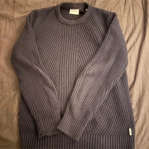 Mörkblå ribbad tröja från Lindbergh - Säljer en stilren mörkblå ribbad tröja från Lindbergh. Tröjan har långa ärmar och en rund halsringning, perfekt för kyligare dagar. Passar bra till både jeans och chinos.