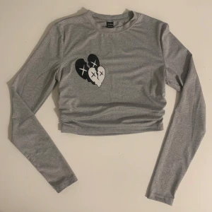 Grå croppad tröja - Säljer en grå croppad tröja från Shein med ett tryck av två hjärtan med korsade ögon. Tröjan har långa ärmar och en rund halsringning. Perfekt för en avslappnad stil