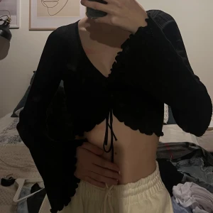 Svart stickad tröja  - Säljer en svart stickad tröja från New Yorker. Tröjan är croppad med knytning framtill och har långa ärmar med volanger. Kommer passa en xxs/xs. Knappt använt! 