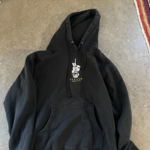 Svart hoodie med tryck - Säljer en svart hoodie med ett unikt tryck på framsidan. Den har en klassisk känguruficka och justerbar huva med dragsko. Perfekt för en avslappnad stil.