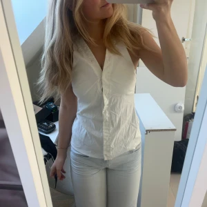 Vit ärmlös blus med knyt i ryggen - Säljer en stilren vit ärmlös blus med v-ringning och knytband i ryggen. 