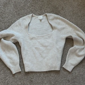 Beige stickad tröja från H&M - Säljer en stilren beige stickad tröja från H&M. Tröjan har en fyrkantig halsringning och långa ärmar, perfekt för kyligare dagar. Den ribbade strukturen ger en snygg och bekväm passform. Passar utmärkt till både jeans och kjol.