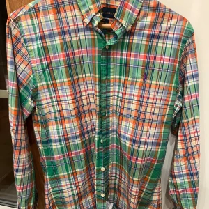 Färgglad rutig skjorta från Ralph Lauren - Säljer en färgglad rutig skjorta från Ralph Lauren i slim fit. Skjortan har en mix av gröna, orangea, blå och vita rutor med en klassisk krage och knappar framtill. Perfekt för att liva upp garderoben!
