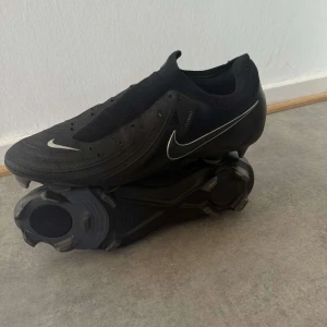 Nike Phantom GX 2 Pro  - Snygga svarta fotbollsskor från Nike med diskret design och klassisk snörning. Perfekta för spel på gräsplaner. Sko snören tillkommer.