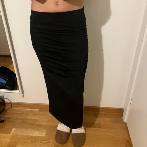Svart långkjol med slits - Snygg svart långkjol med slits på sidan. Kjolen har en tight passform och är perfekt för en stilren look. Den är gjord i ett mjukt och bekvämt material som formar sig fint efter kroppen.
