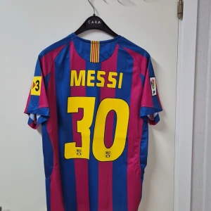 FC Barcelona Messi 30 matchtröja Nike - Säljer en klassisk FC Barcelona fotbollströja med Messi och nummer 30 på ryggen. Tröjan är blå och röd med gula detaljer, randigt mönster och klubbmärke på bröstet. Tillverkad i lätt och ventilerande material, perfekt för dig som älskar fotboll och Barca.