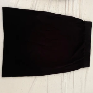 Svart långkjol i bomull - Enkel svart kjol med rak passform och bred resår i midjan. Kjolen är tillverkad i mjuk bomull och passar perfekt för en clean och stilren look. Lätt att matcha med olika toppar och sneakers.