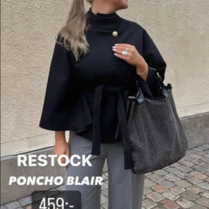 Mörkblå ponchojacka trendig från Blair missäy - Stilren mörkblå ponchojacka från Blair med hög krage, knytbälte i midjan och en snygg guldig knapp vid halsen. Jackan har vida ärmar och en loose passform som ger en cool och avslappnad vibe. Perfekt att slänga över en outfit för extra edge.