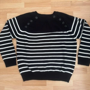 Ny. Svartvit randig stickad tröja L - Svart och vit randig stickad tröja i storlek L med snygga knappar på axlarna. Tröjan har rund halsringning, långa ärmar och ribbade muddar. Perfekt för dig som gillar klassisk stil med en twist. Tröjan är bara tvättat för jag tvättar alltid nya plagg, men hade aldrig på mig.