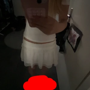 Vit volangkjol  - Supersöt vit kortkjol med volanger och bred smock i midjan. Kjolen är luftig och har en lätt, flowy känsla som passar perfekt till varma dagar. 