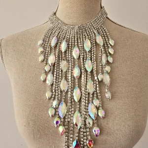 Statement halsband med glittriga stenar - Superblingigt statement halsband med stora, droppformade prismastenar och massor av gnistrande strass i silverfärg. Halsbandet har en bred krage och långa hängande kedjor som ger en riktigt lyxig och iögonfallande look.