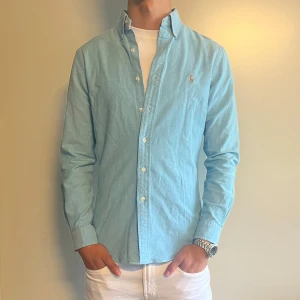 Ljusblå skjorta från Ralph Lauren - Snygg ljusblå skjorta från Polo Ralph Lauren i slim fit stretch oxford. Klassisk button-down krage, broderad logga på bröstet och vita knappar. Perfekt för dig som gillar stilrena och fräscha plagg med skön passform. I storlek M