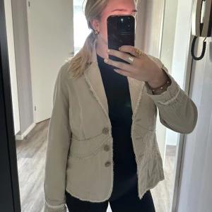 Beige kavaj med broderade detaljer - Säljer en beige kavaj med snygga broderade detaljer och råa kanter. Jackan har dekorativa knappar framtill och markerad midja. Långärmad modell med coola sömmar och unik struktur. Perfekt för dig som vill ha en stilren men ändå speciell look. Storlek 44 men passar som M🤗🥰