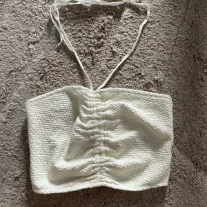 Vit linnetopp från & Other Stories - Superfin vit linnetopp från & Other Stories med smockad struktur och knytband i nacken. Toppen har snygg rynkdetalj framtill och är ärmlös, perfekt för varma dagar. Materialet känns mjukt och luftigt mot huden.