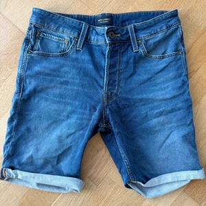 Blå jeansshorts från Jack & Jones - Snygga blå jeansshorts från Jack & Jones i regular fit. Klassisk femficksmodell med uppvikta benslut, bälteshällor och dragkedja. Perfekta för sommardagar och enkel att matcha med t-shirt eller hoodie.