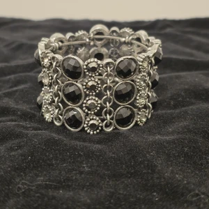 Brett armband med svarta stenar - Coolt och brett armband i silverfärgad metall med stora svarta, facetterade stenar och kedjedetaljer. Armbandet har en vintagekänsla och är perfekt för att ge outfiten en edgy touch.