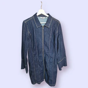 Jeansklänning i storlek 46 från Kappahl - Mörkblå jeansklänning med lång ärm och dragkedja framtill. Klänningen har en krage och dekorativa sömmar. Endast använd en gång.