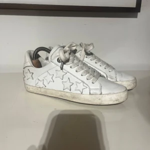 Vita sneakers med stjärnor Zadig & Voltaire 38 - Snygga vita sneakers från Zadig & Voltaire i skinn med coola stjärndetaljer på sidorna. Klassisk låg modell med snörning och rund tå. Perfekta för dig som gillar en stilren men ändå lekfull look. Stolek 38
