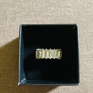 Mix av ring, örhängen och armband - Säljer ett set med smycken: en bred ring i guldton med rektangulära stenar, ett par hjärtformade örhängen med glittriga stenar och pärldetaljer, ett armband i tre färger (guld, silver, koppar) samt två par örhängen i silver, ett par hjärtformade och ett par stavformade med små stenar.