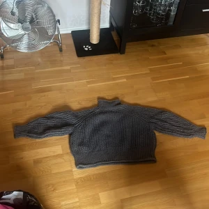 Grå stickad polotröja - Mysig grå stickad polotröja med bred ribbstickning och lång ärm. Tröjan har en hög krage och en loose passform som ger en avslappnad vibe. Perfekt för kyliga dagar när du vill vara både bekväm och snygg.