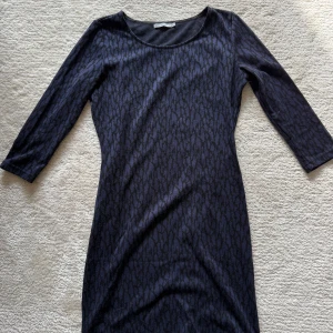 Mörkblå mönstrad klänning Soaked in Luxury - Snygg mörkblå kortklänning från Soaked in Luxury med diskret mönster och trekvartsärm. Klänningen har en rund halsringning och figurnära passform, perfekt för dig som gillar stilrena och bekväma plagg.