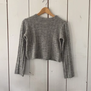 Grå croppad stickad tröja Divided - Mysig grå croppad stickad tröja från Divided by H&M. Tröjan har långärmade ribbade ärmar och en enkel rund halsringning. Perfekt för lager-på-lager och passar till både jeans och kjol.
