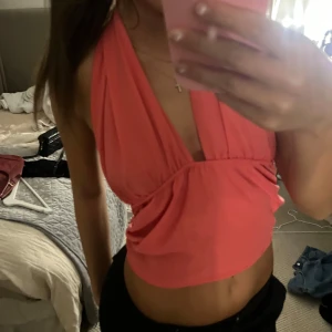 Rosa omlott halterneck croppad topp - Säljer en rosa croppad halterneck topp med omlott-skärning och knyt i nacken. Toppen har öppen rygg och smockad detalj baktill för extra komfort. Perfekt för varma dagar och snygg att styla med jeans eller kjol.