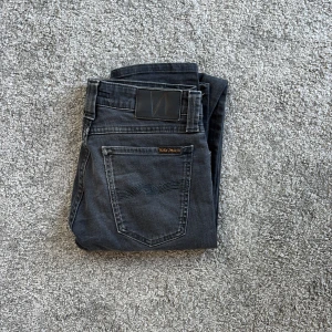 Svarta jeans från Nudie Jeans - Snygga svarta jeans från Nudie Jeans med klassisk femficksdesign och diskreta sömmar på bakfickorna. Jeansen har en rak passform och är tillverkade i mjukt denimtyg av bomull. Perfekta för en stilren och avslappnad look.