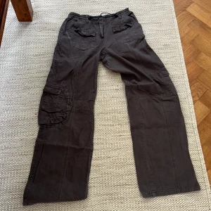 Grå cargopants från Brandy Melville - Säljer ett par grå cargopants från Brandy Melville med flera fickor och dragsko i midjan. Byxorna har en loose passform och är tillverkade i bomull, perfekta för en avslappnad streetstyle-look.