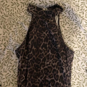 Leopardmönstrad ärmlös topp - Snygg ärmlös topp med leopardmönster i mörka toner. Hög halsringning och smickrande passform, perfekt för att sticka ut. Materialet känns mjukt och följsamt mot huden.