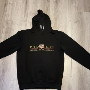 Svart hoodie från Vinson Polo Club - Svart hoodie från Vinson Polo Club med tryck i gult och vitt på bröstet. Klassisk luva, känguruficka och ribbade muddar. Snygg och enkel stil som funkar till jeans eller joggers. Materialet känns mjukt och bekvämt mot huden.