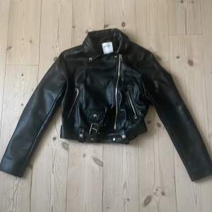 Svart skinnjacka från Bershka  - Snygg svart skinnjacka från Bershka i klassisk bikerstil. Jackan har silvriga dragkedjor, bälte i midjan och coola detaljer som snedställd dragkedja och fickor med dragkedja.upplevs däremot liten i storlek skulle mer säga som M än L. Väldigt bra skick då den har använts max 3 ggr.
