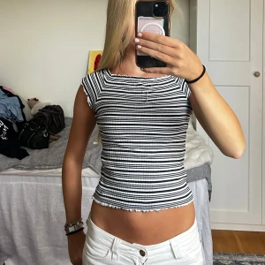 Randig topp med volangkant - Superfin ribbad topp med mörkblå och vita ränder. Modellen är tight och har korta ärmar samt volangkant vid ärmslut och nederkant. Perfekt till jeans eller kjol för en enkel men snygg outfit. Passar mig som vanligtvis har xs/s.