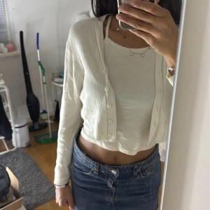 Vit croppad kofta från Lindex - Säljer en vit, ribbad och croppad kofta från Lindex. Koftan har långa ärmar, knappar framtill och är tillverkad i mjuk bomull. Perfekt att slänga över ett linne eller t-shirt för en chill och stilren look.