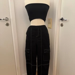 Svarta cargopants med vita sömmar stl 140 - Svarta cargopants med kontrasterande vita sömmar och elastisk midja. Stl 140. Nya! Byxorna har stora fickor på sidorna och resår vid bensluten och loose passform. Hämtas på Hägerstensåsen eller skickas. 