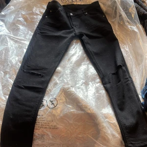 Svarta superslim jeans W.BXTR strl 32 - Svarta jeans från W.BXTR i modellen Tim Superslim. Byxorna har smal passform, slitna detaljer vid knäna och klassisk femficksdesign. Tillverkade i bomull med lite stretch för extra komfort. Perfekta för dig som gillar en tajt och modern look.