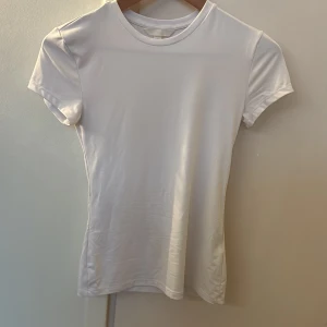 Vit basic t-shirt från H&M - En klassisk vit t-shirt från H&M i storlek S. Modellen är figurnära med rund halsringning och korta ärmar. Perfekt att styla med jeans eller kjol för en clean look. Gjord i mjuk bomull som känns skön mot huden.