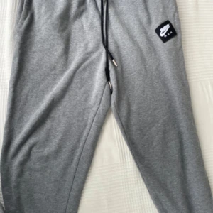 Gråa Jordan mjukisbyxor med snörning - Säljer ett par gråa mjukisbyxor från Jordan med elastisk midja och svart snörning. Byxorna har standard fit, sidofickor och den klassiska Jumpman-loggan på benet. Perfekta för chill eller sportiga dagar.