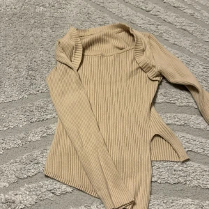 Beige ribbad långärmad tröja - Snygg beige ribbad tröja med lång ärm och rundad hals. Tröjan har en figurnära passform och är tillverkad i ett stretchigt stickat material. Perfekt att styla med jeans eller kjol för en trendig look.