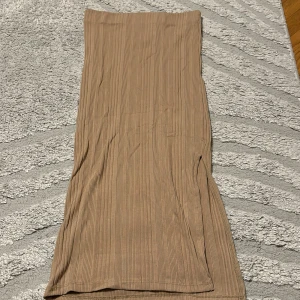 Beige ribbad långkjol med slits - Säljer en beige långkjol med ribbad struktur och en snygg slits på sidan. Kjolen har en rak passform och är perfekt för dig som gillar en stilren och enkel look. Superenkel att matcha med både sneakers och boots.